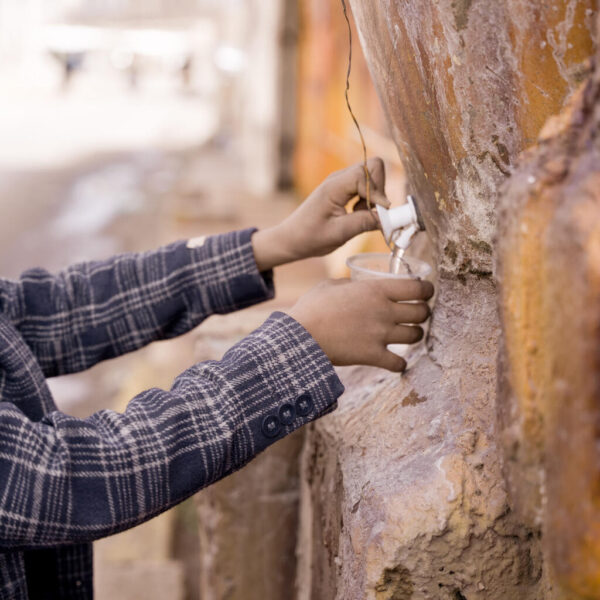 A child fills a plastic cup with water from a public clay cooler.