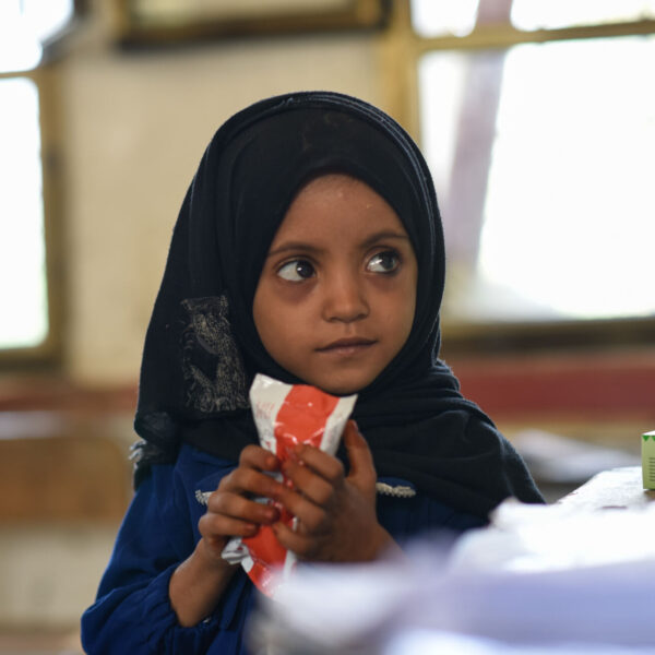 Four-year-old Jihan grips a packet of nutritious food in her hand and looks off-camera.