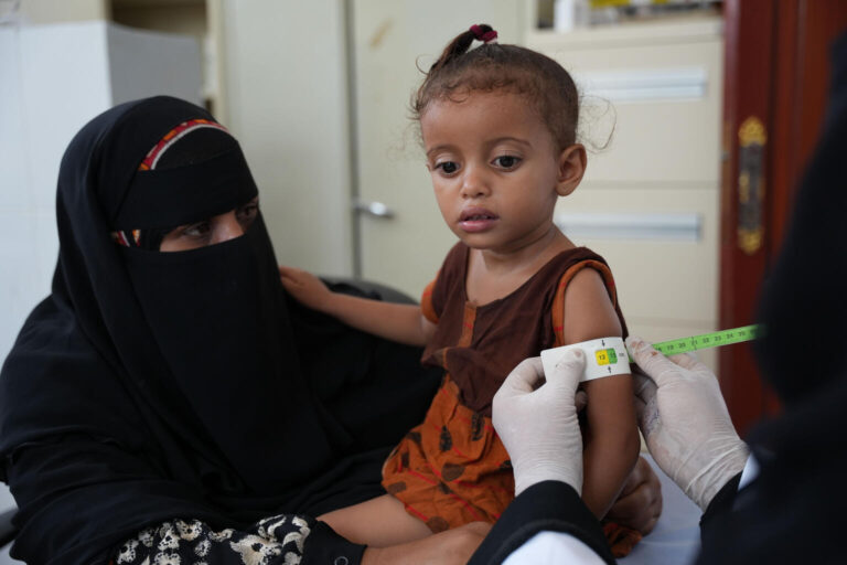 Radhya, young girl in Yemen, has her arm measured with a strip of tape by a doctor in a UNICEF-implemented nutrition service.