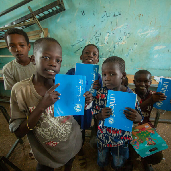 A group of children hold their UNICEF-blue exercise books up.