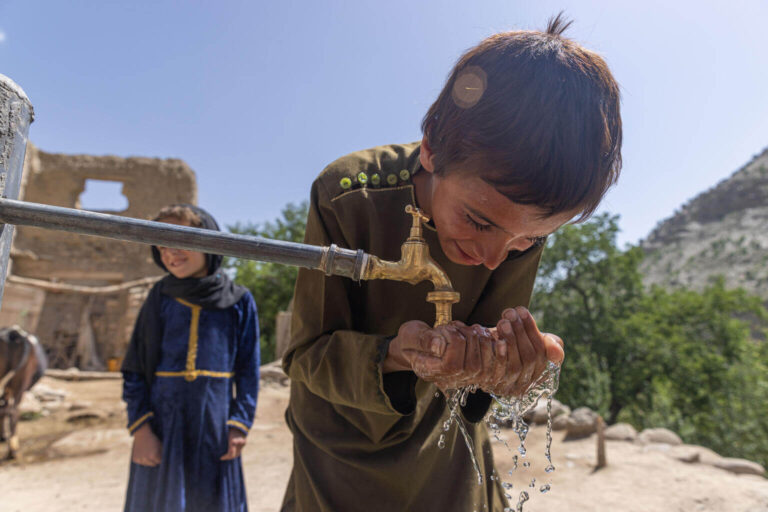 A 9 years old washes his hands at a new water tap at his home, with his 6 years old sister, behind him.