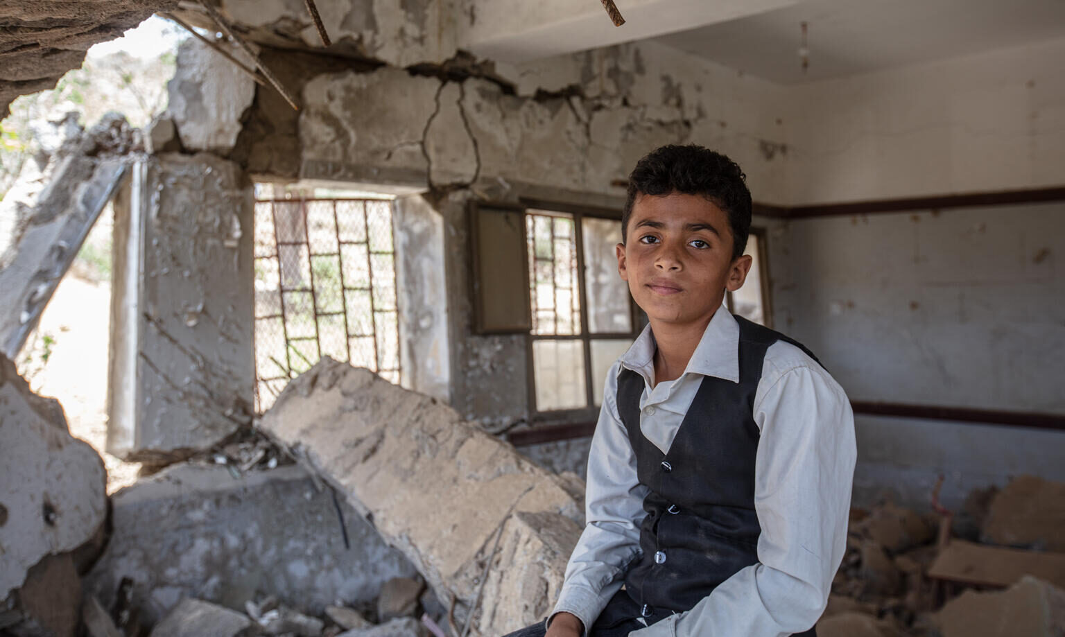 12-year-old Ahmed sits on the rubble of his school in Hajjah, Yemen.