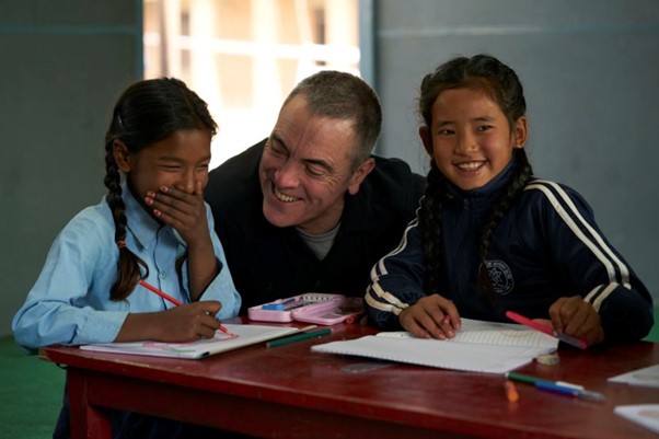 A UNICEF ambassador in a classroom with two children laughing.