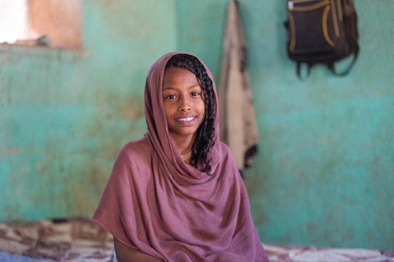 Samar sits in the classroom where she now lives, smiling.