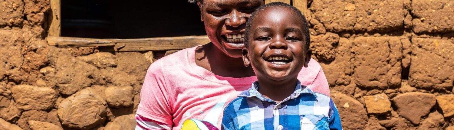 A mother and child smile and laugh while sitting in front of their house.