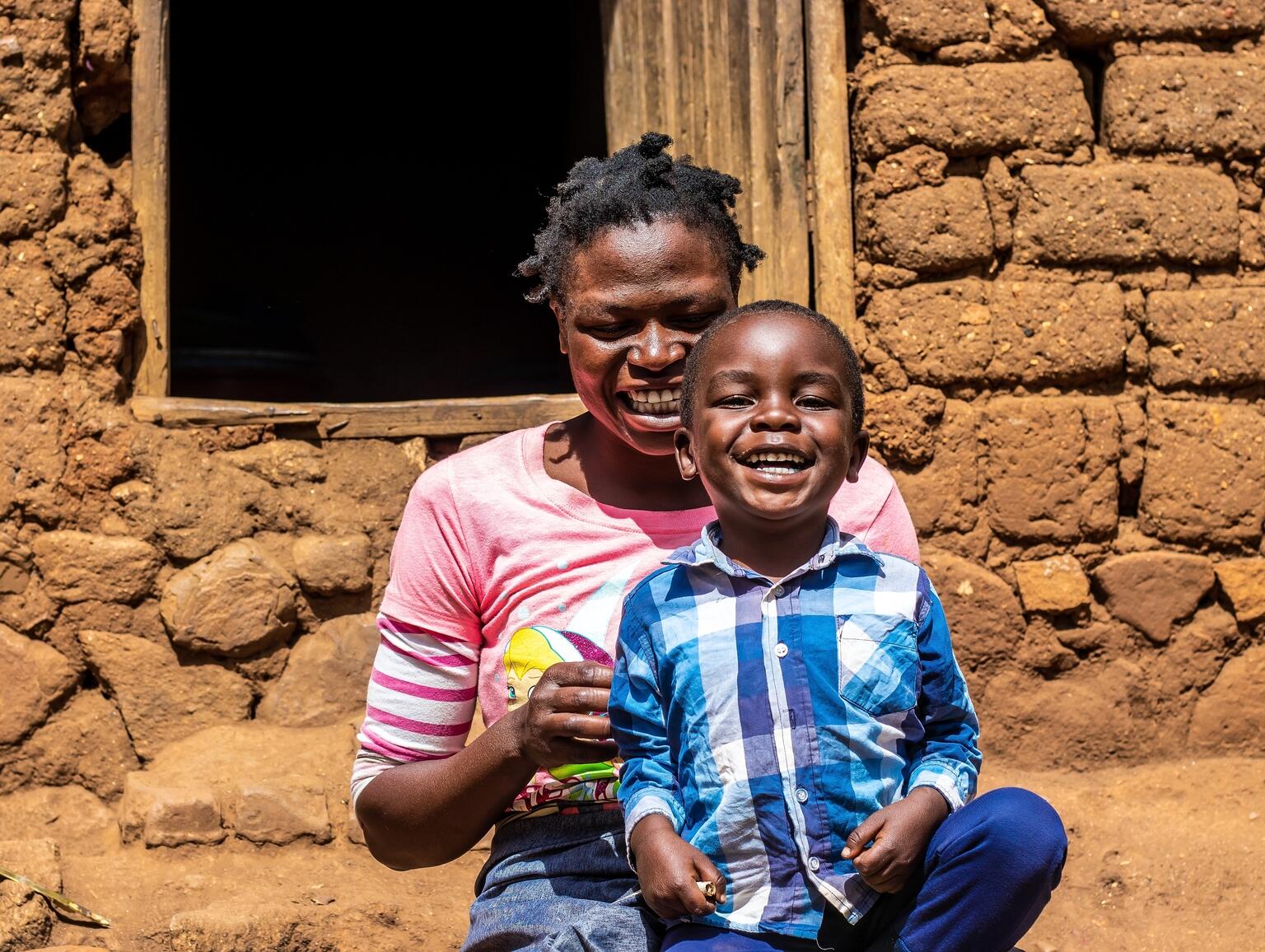 A mother and child smile and laugh while sitting in front of their house.