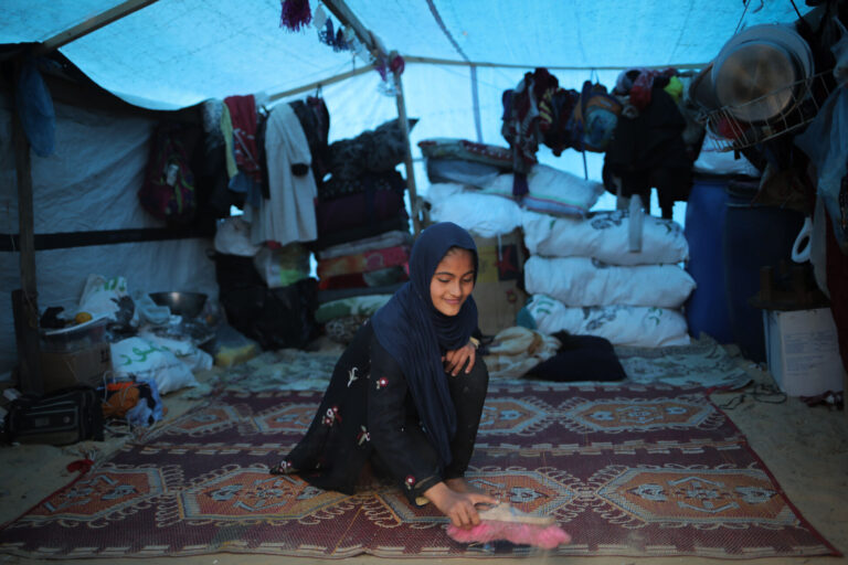 14 year old girl Duha puts on an optimistic smile in her makeshift tent while displaced in Rafah, The State of Palestine.