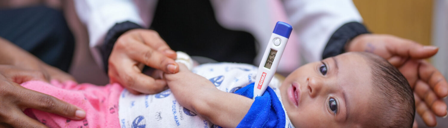 4-month-old baby boy Sanad is held by his mother, Raneem, while having his temperature taken during an examination by a health worker in the Therapeutic Feeding Centre (TFC), of Ibn Khaldoun Hospital in Al Hawtah, Lahj Governate, Yemen.