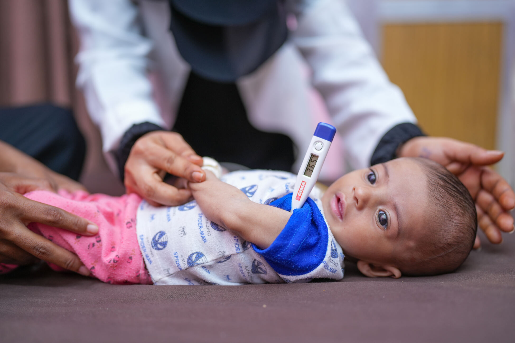 4-month-old baby boy Sanad is held by his mother, Raneem, while having his temperature taken during an examination by a health worker in the Therapeutic Feeding Centre (TFC), of Ibn Khaldoun Hospital in Al Hawtah, Lahj Governate, Yemen.